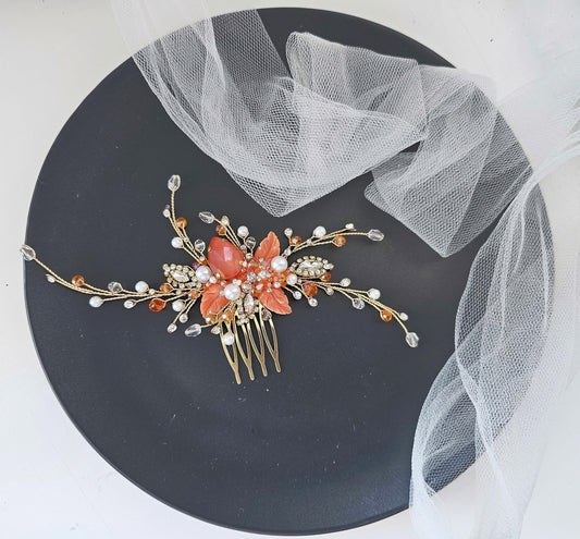 A decorative hair clip with a floral design and sparkling gemstones rests on a black plate, accompanied by a white net or veil.