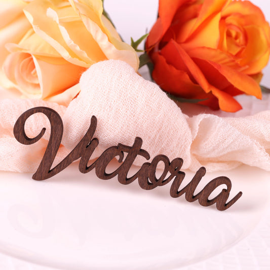 a wooden nameplate with the name "Victoria" written on it, placed on a white surface next to two roses.
