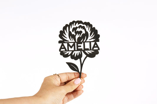 A hand holding a paper cutout of a flower with the name "Amelia" written on it.