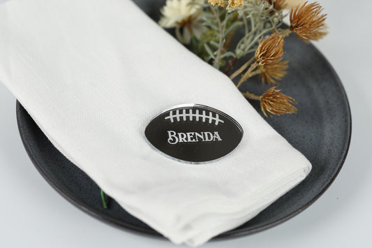 A white napkin with a black oval-shaped nameplate on it, placed on a black plate.
