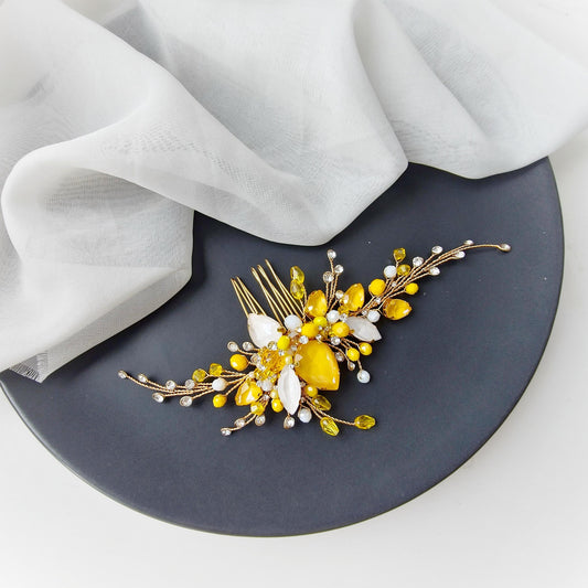 A decorative hair accessory with yellow and white elements, such as flowers and stones, is placed on a black plate.