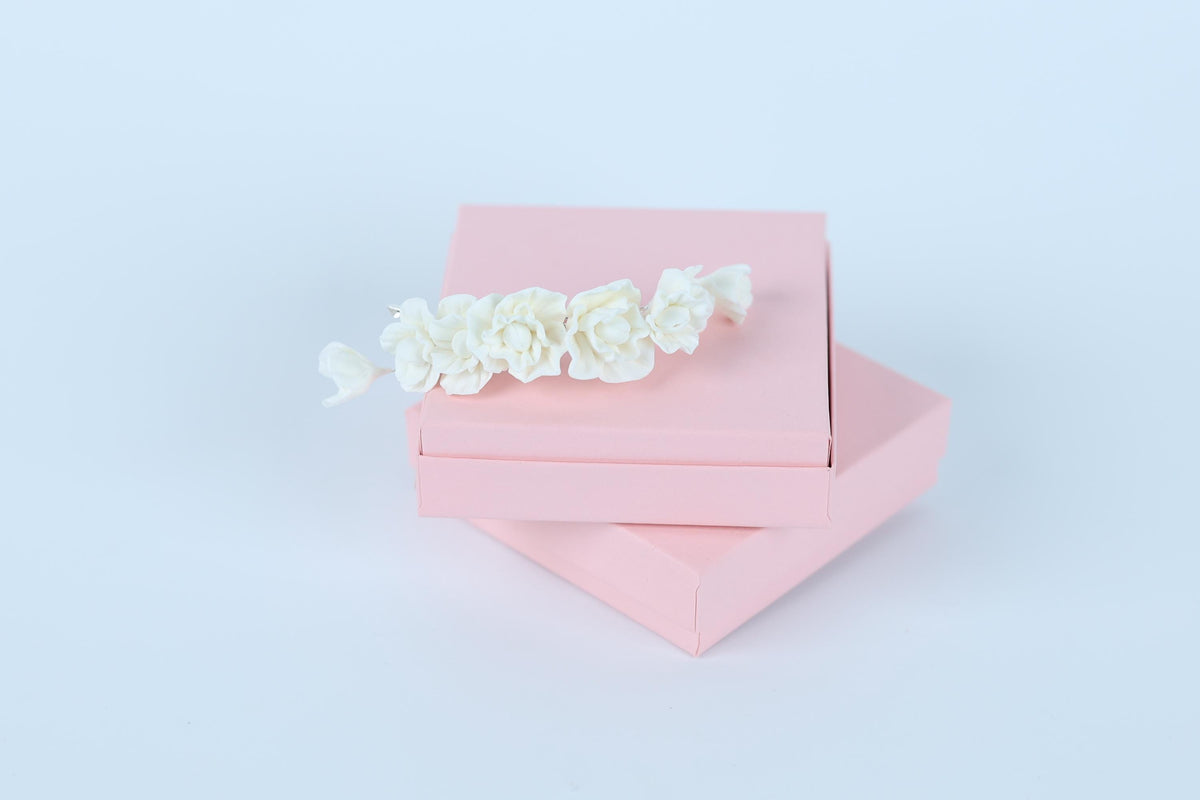 A pink gift box with a delicate white flower decoration on top, set against a plain white background.
