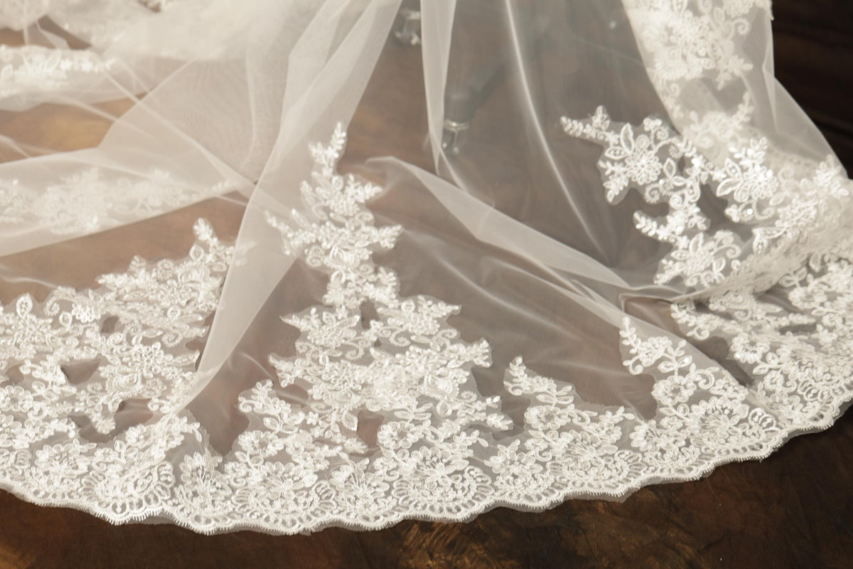 A close-up view of a delicate, white lace veil with intricate floral embroidery.