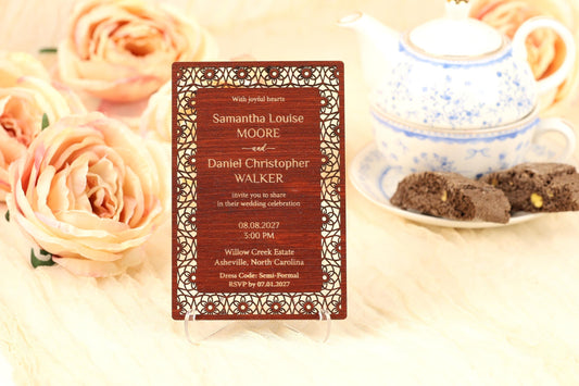 A wooden wedding invitation card with a floral design, placed on a table with a teapot and some pastries in the background.