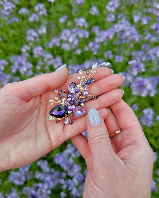 a woman's hand holding a purple flower brooch