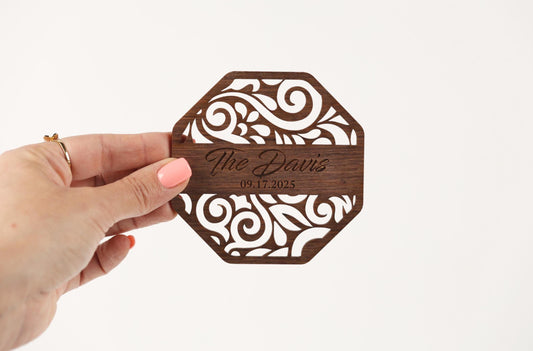 A hand holding a wooden coaster with a decorative design and text on it.