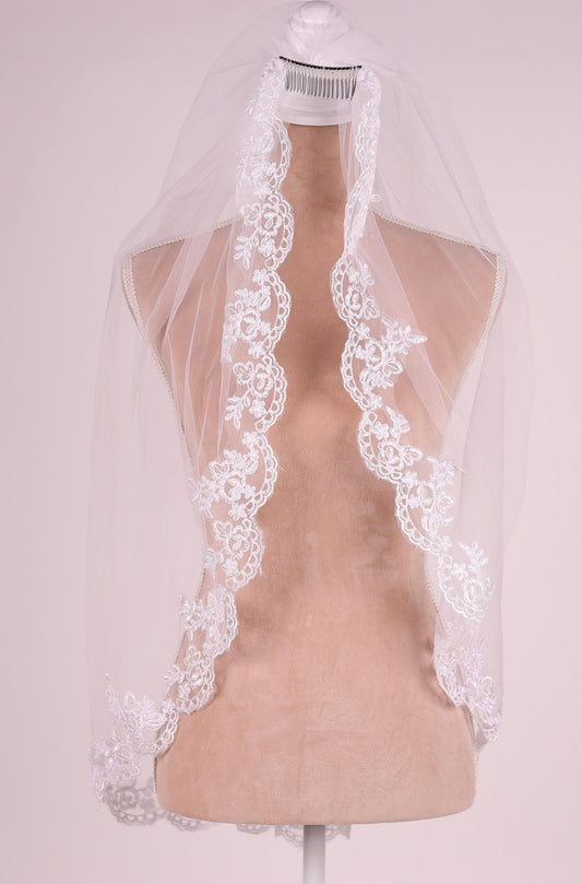 A white wedding veil with a delicate lace trim is displayed on a mannequin.