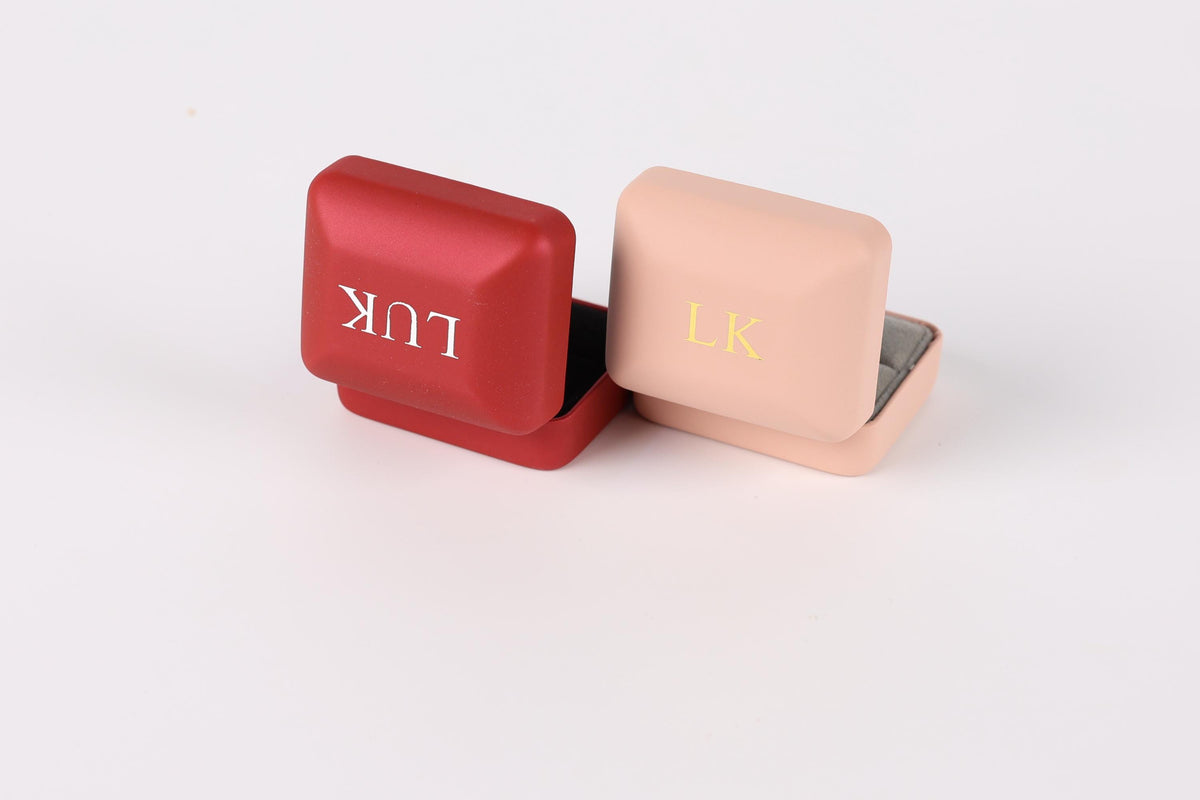Two small metal jewelry boxes, one red and one pink, with the letters "LK" printed on them.