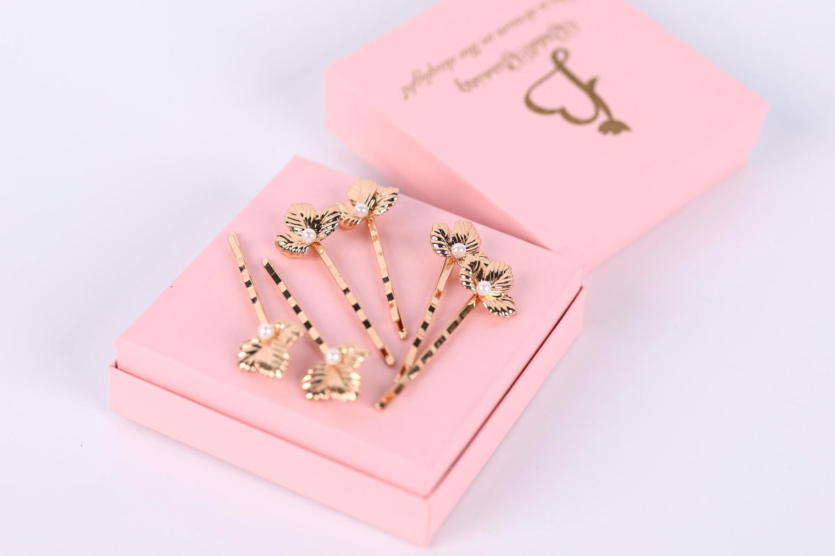 A pink box containing several gold-colored hair clips with floral designs.