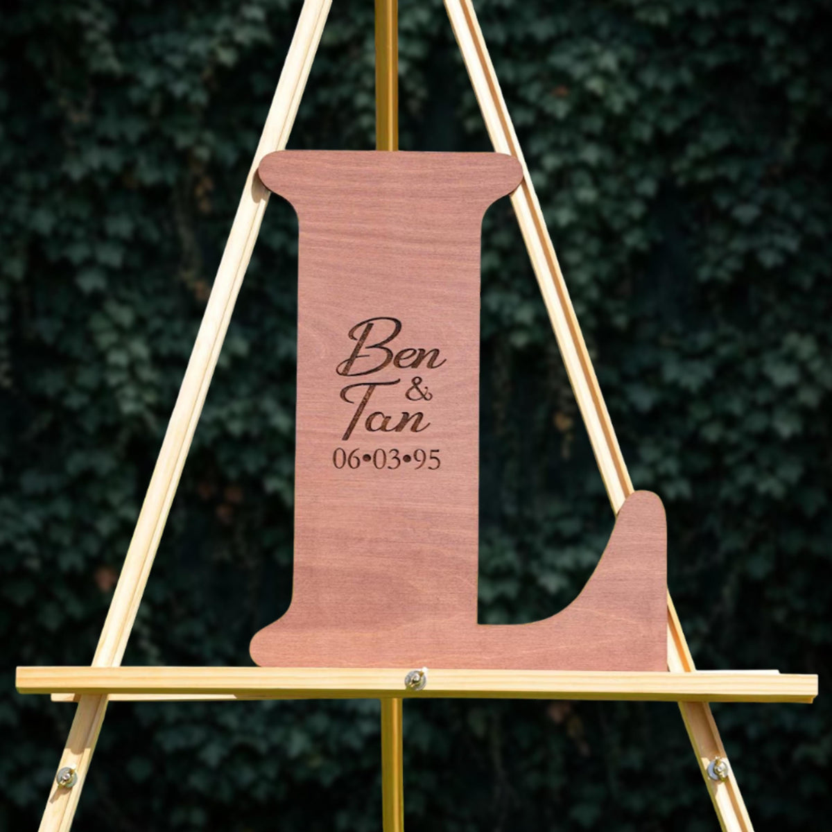 A wooden letter 'L' on a stand, with the names 'Ben & Tan' and the date '06-03-95' engraved on it.