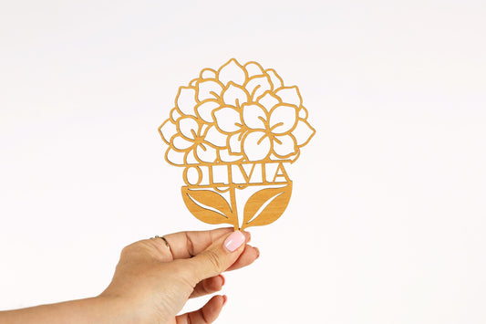 A hand holding a paper cutout of a flower with the name "Olivia" written on it.