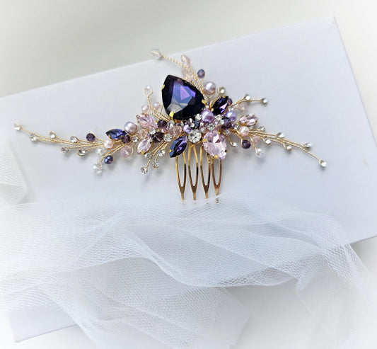 A decorative hair clip with a floral design and a large purple gemstone on top, placed on a white background.