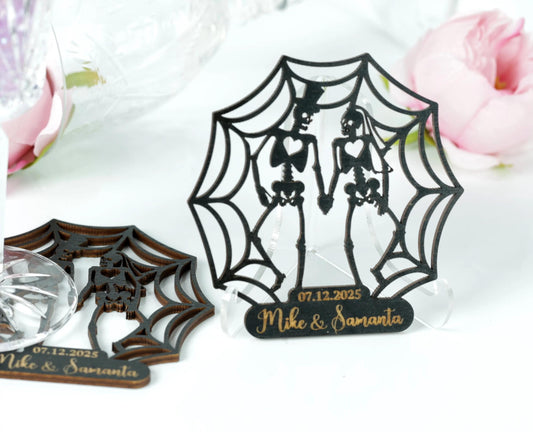 a couple of custom-made wedding or anniversary decorations, including a spider web-like design and a wooden frame with a couple's silhouette. The decorations are placed on a white surface, with a pink flower in the background.