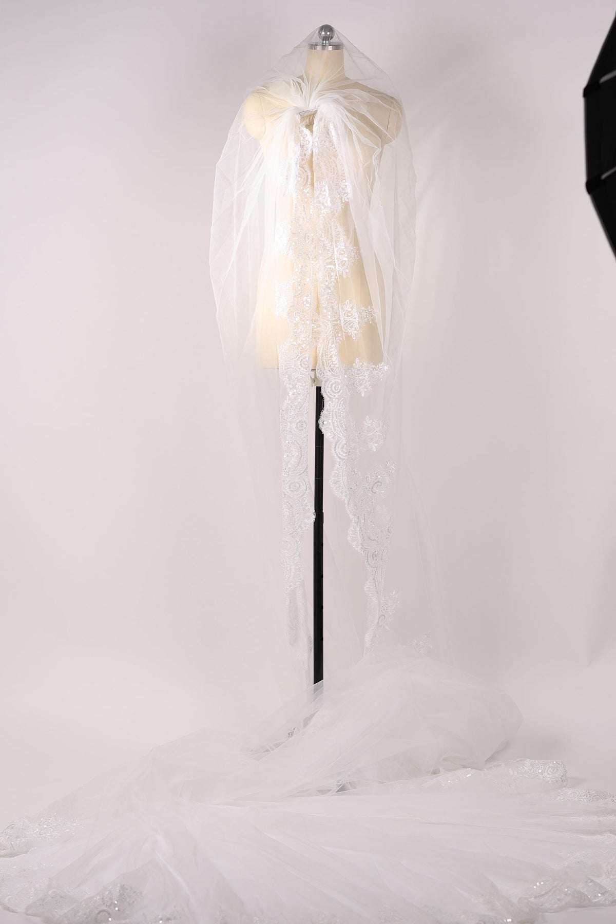 A white wedding dress with a veil is displayed on a mannequin, with the veil blowing in the wind.
