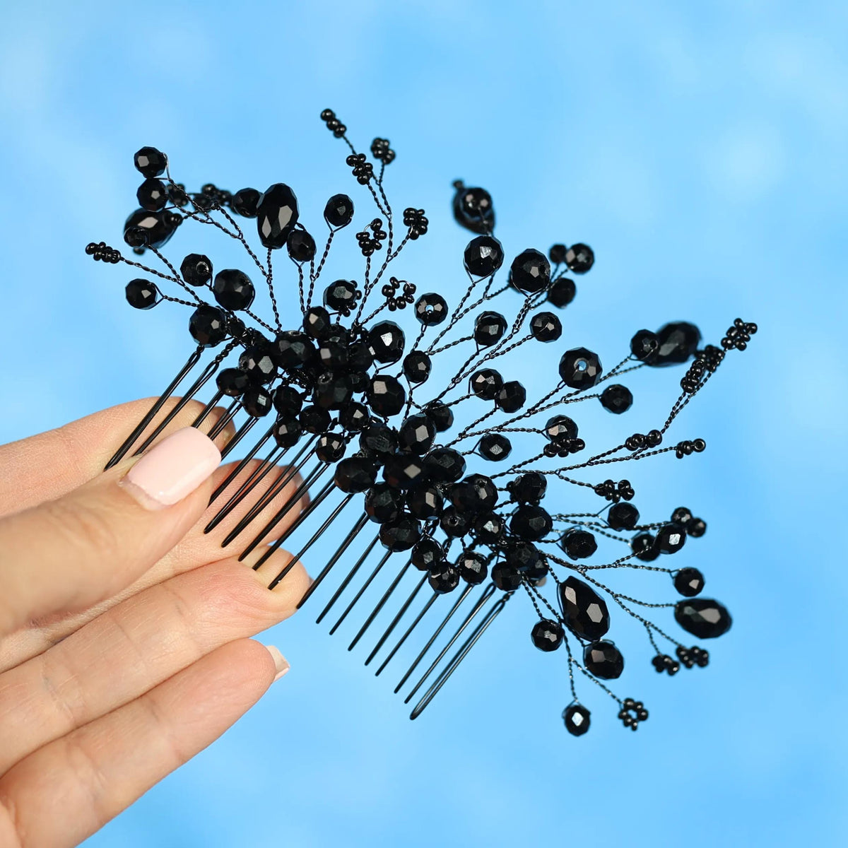 A hand holding a black hair accessory with black beads against a blue background.