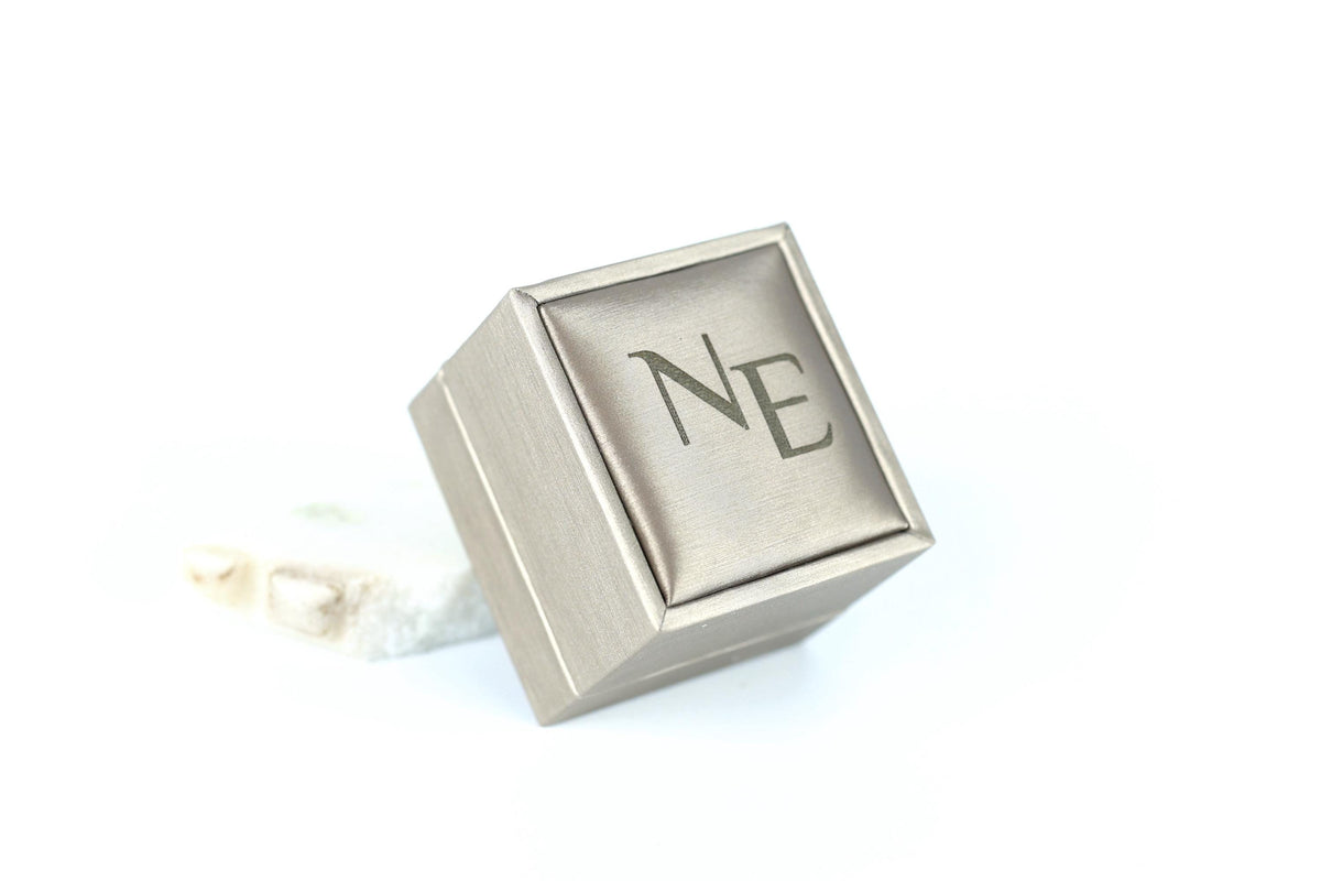 A silver-colored box with the letters "NE" embossed on it, sitting on a white surface.