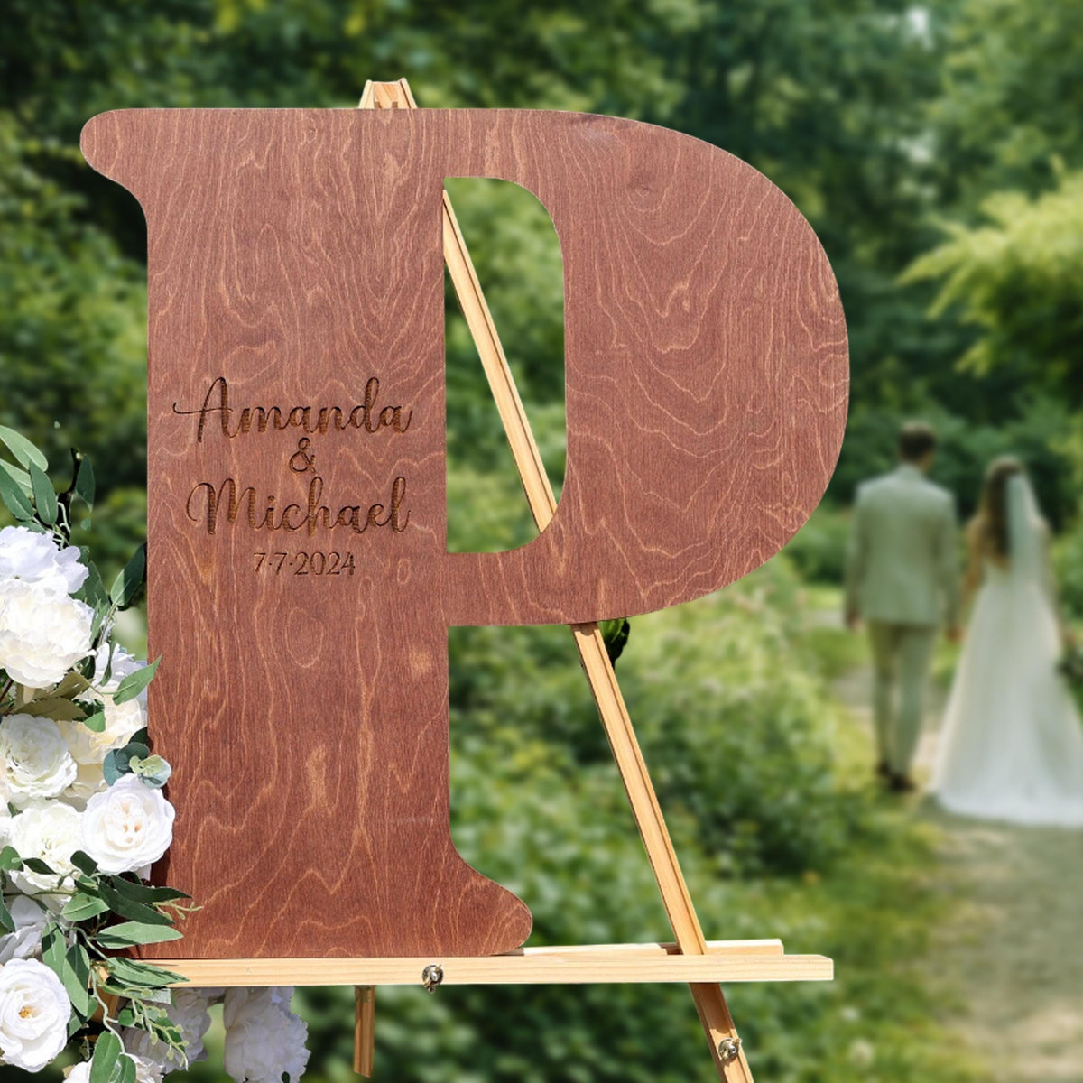 A wooden sign with the initials "P" and the names "Amanda & Michael" engraved on it, standing in a garden setting with a couple walking in the background.