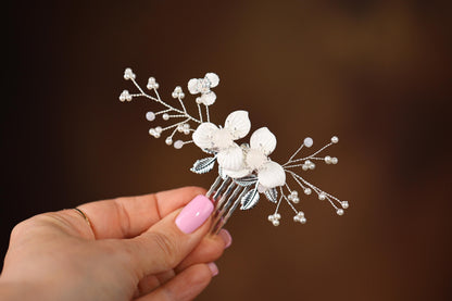 a hand holding a white flower and pearl hair comb