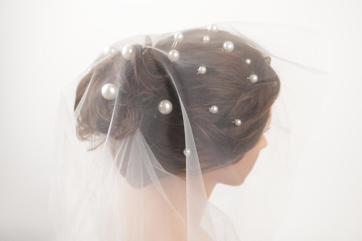 A close-up of a woman's head wearing a veil with small white pearls attached to it.