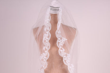 A mannequin wearing a white lace wedding veil with a floral pattern.