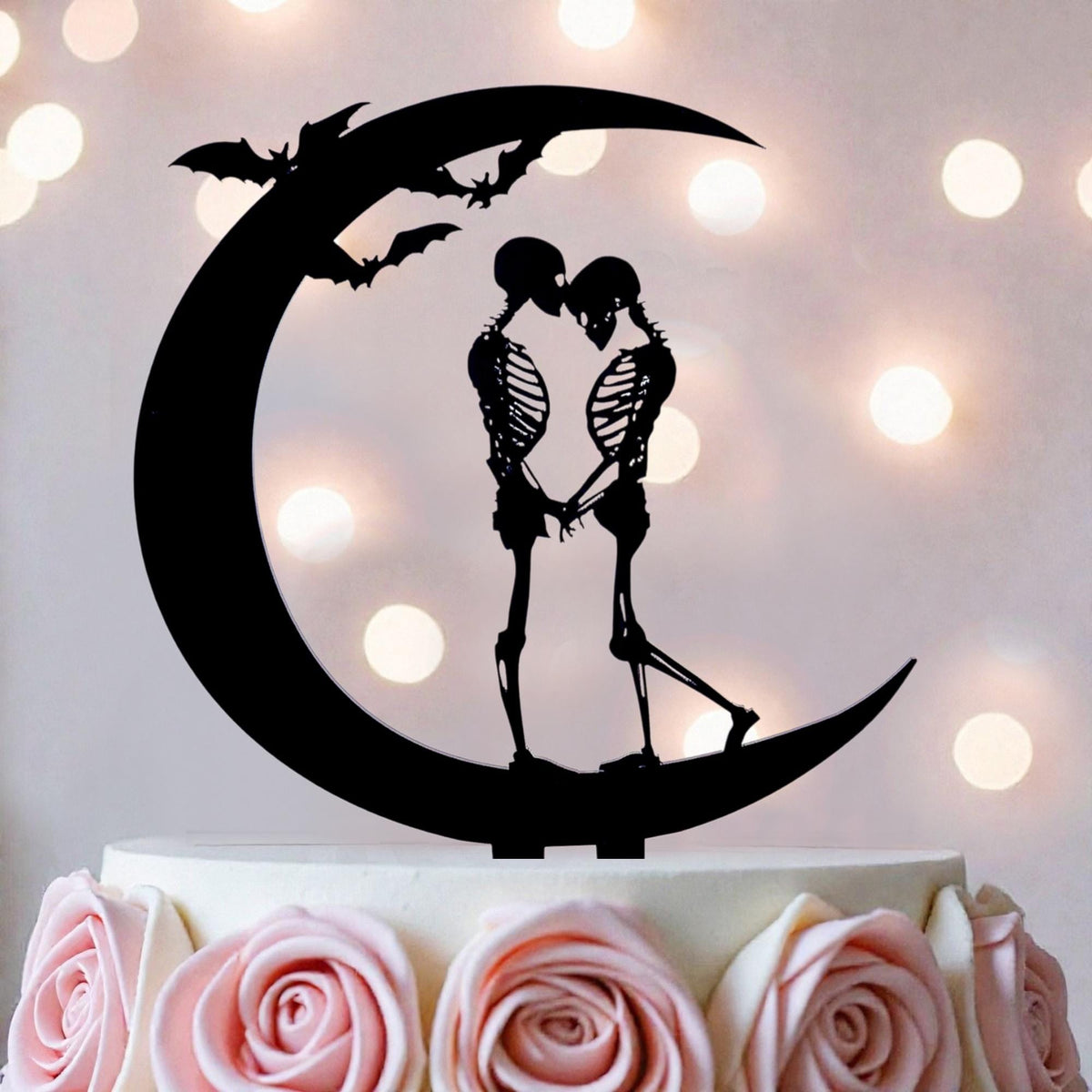 A black silhouette of a skeleton couple embracing on a crescent moon, with bats flying above them, is the central focus of the image.