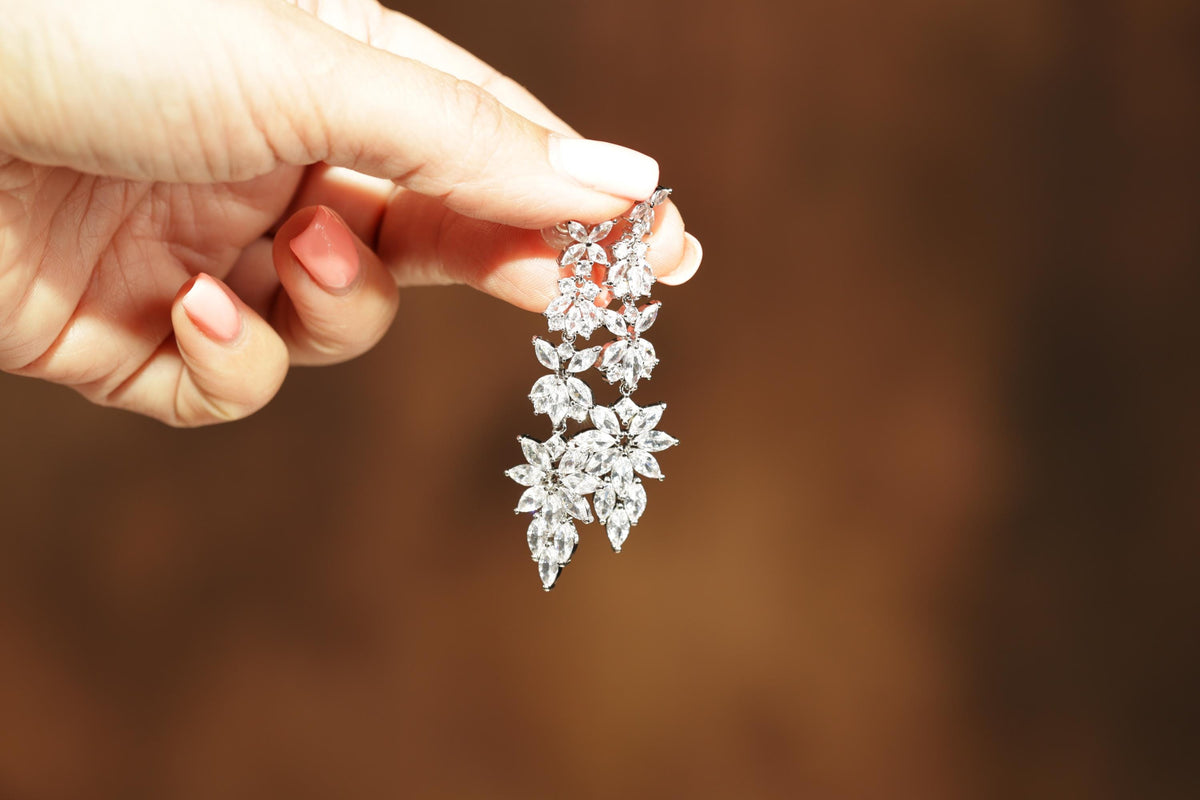 A hand holding a delicate, sparkling diamond earring against a blurred brown background.