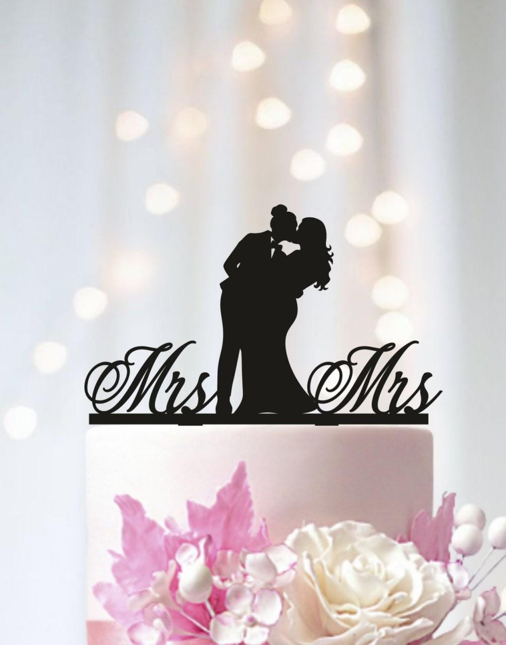 A silhouette of a bride and groom on a wedding cake topper, with the words "Mrs. Mrs." written below.
