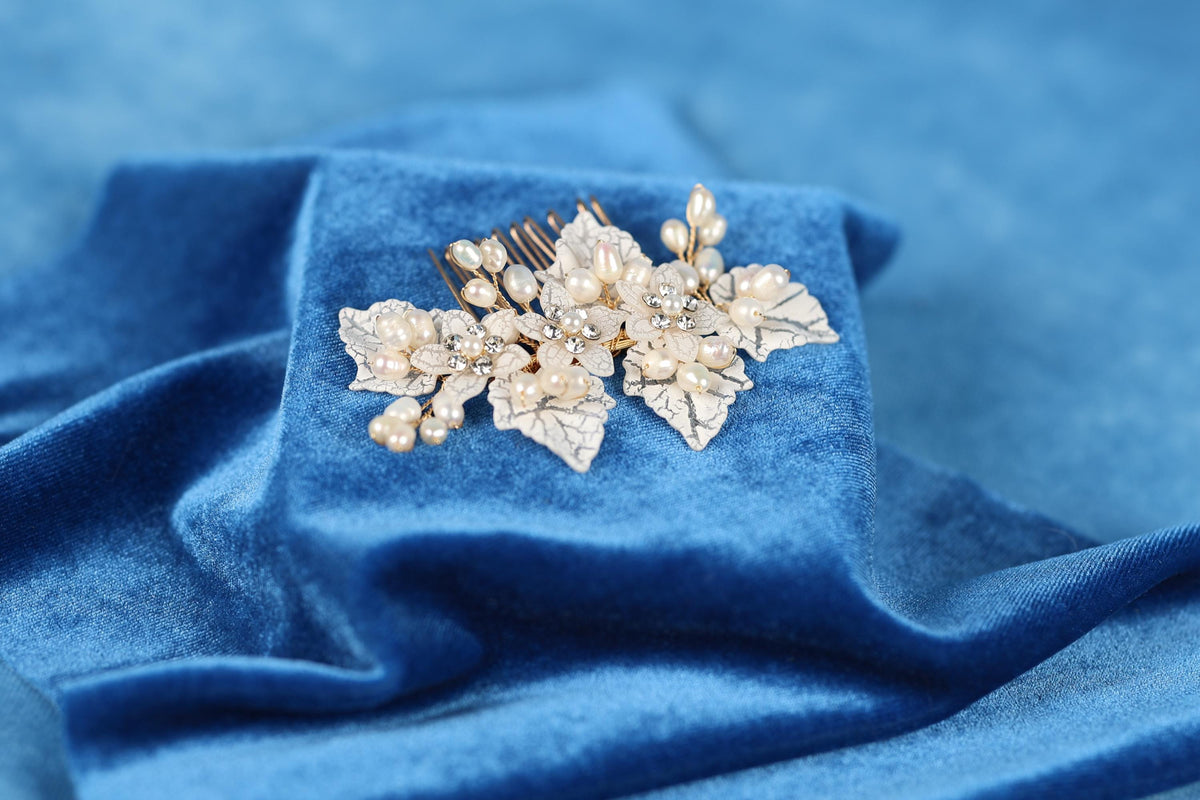 A decorative hair accessory with white flowers and pearls rests on a blue fabric surface.