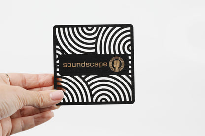 A hand is holding a square-shaped object with a black and white striped pattern and the word "soundscape" written on it.