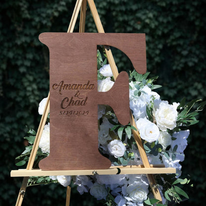 a wooden letter 'F' with a floral arrangement of white flowers behind it.