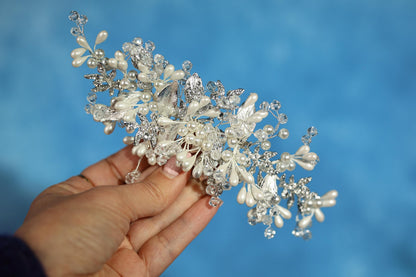 A hand holding a decorative piece of jewelry against a blue background.