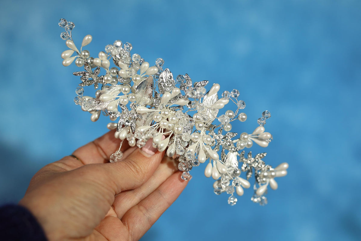A hand holding a decorative piece of jewelry, which appears to be a bracelet or headband, against a blue background.