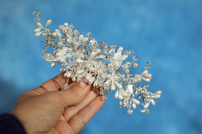 A hand holding a decorative piece of jewelry, which appears to be a bracelet or headband, against a blue background.