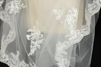 A close-up view of a delicate, white lace veil with intricate floral embroidery.