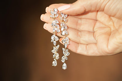A hand holding a pair of elegant diamond earrings with multiple tiers of sparkling stones.