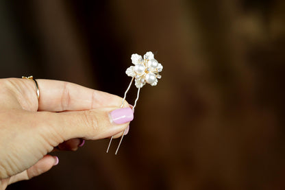 A hand holding a small, ornate piece of jewelry, possibly a flower-shaped pendant or brooch, against a blurred background.