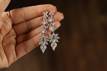 A hand holding a pair of elegant diamond earrings against a blurred background.