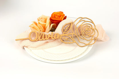 A wooden nameplate with the name "Olivia" carved into it, accompanied by two orange roses on a white background.