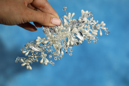 A hand holding a decorative piece of jewelry, which appears to be a bracelet or headband, against a blue background.