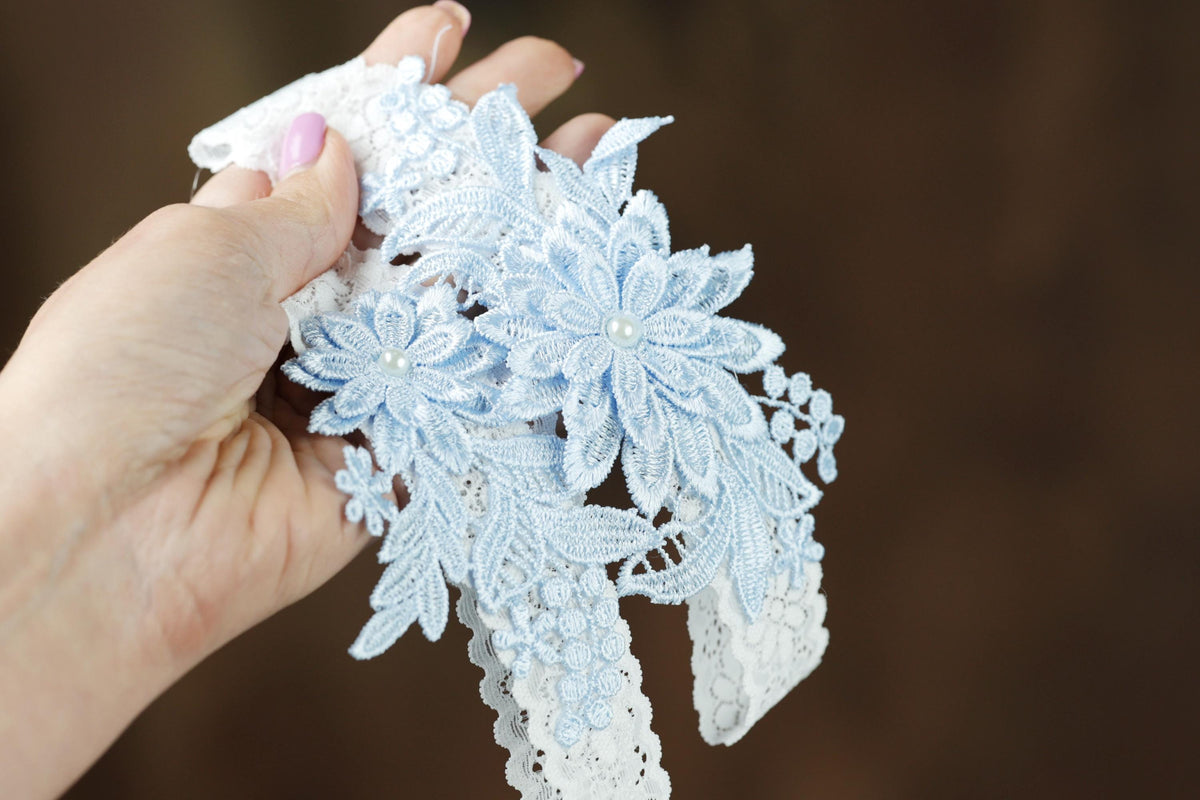 A hand holding a piece of delicate, intricately embroidered lace against a blurred background.