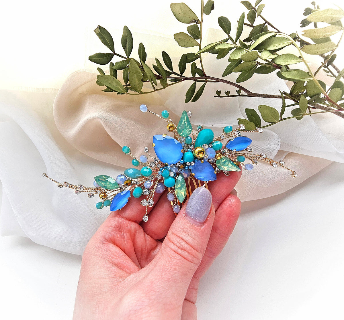 a hand holding a blue and green flower brooch