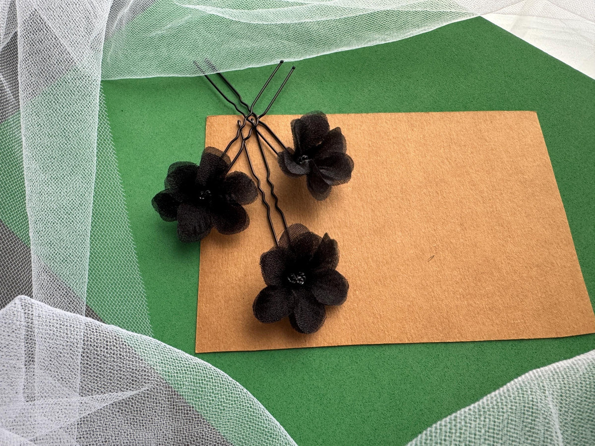three black flower-shaped hair clips arranged on a brown paper sheet against a green background.