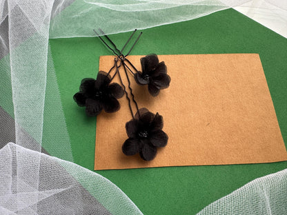 three black flower-shaped hair clips arranged on a brown paper sheet against a green background.