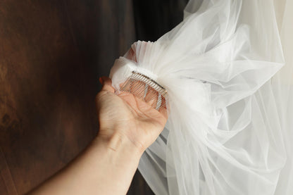 A hand holding a white veil with a decorative metal clasp.