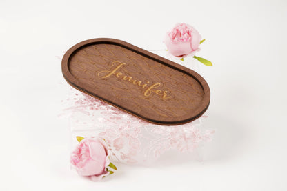 a wooden tray with the name "Jennifer" engraved on it, placed on a clear stand with two pink roses.