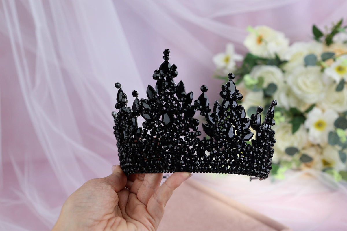 a hand holding a black tiara next to a bouquet of flowers