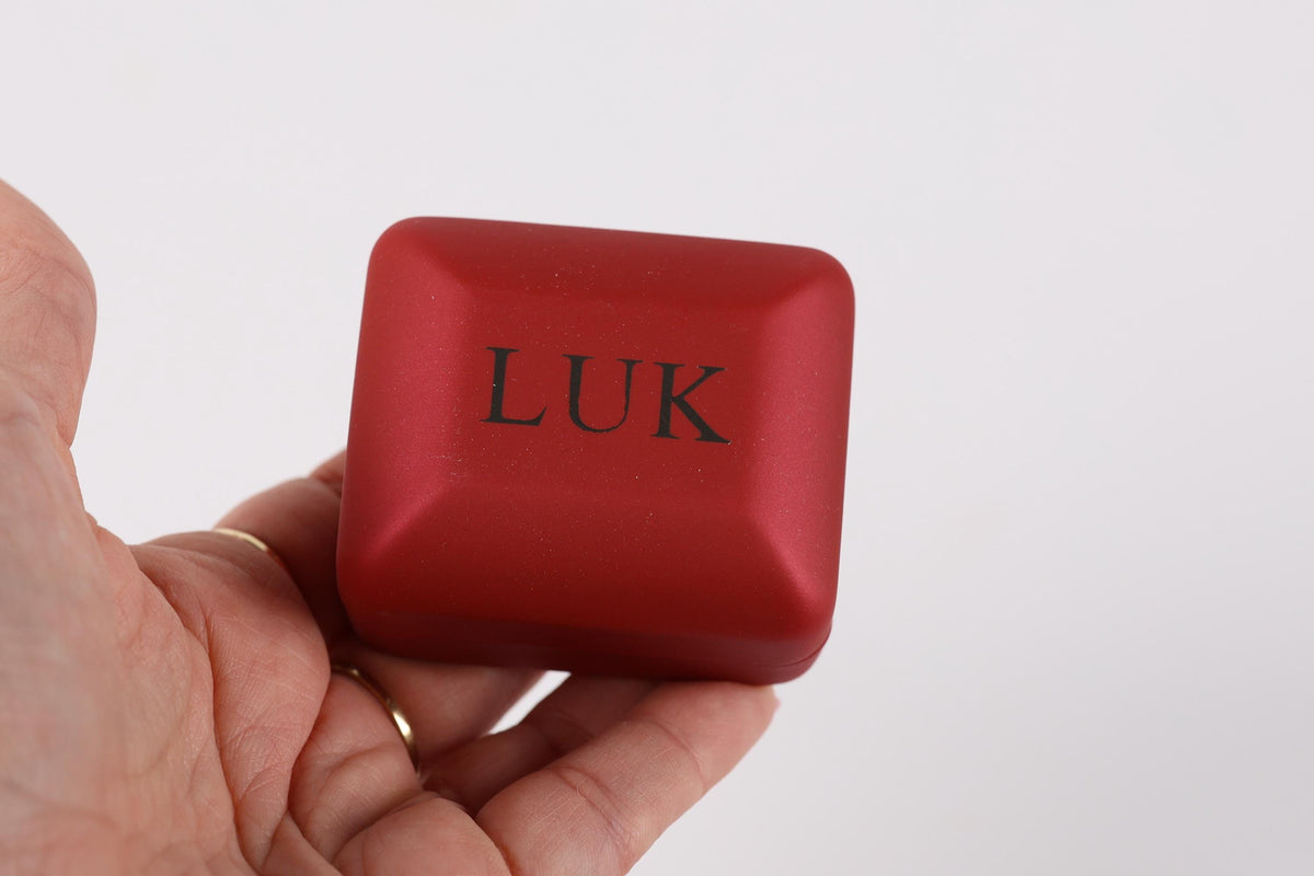 A hand holding a red, square-shaped object with the word "LUK" printed on it.