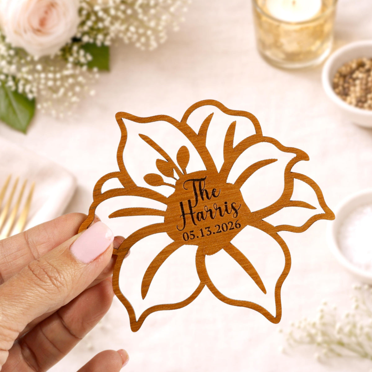 A hand holding a wooden flower-shaped card with the name 'The Harris' and the date '05.15.2026' printed on it.