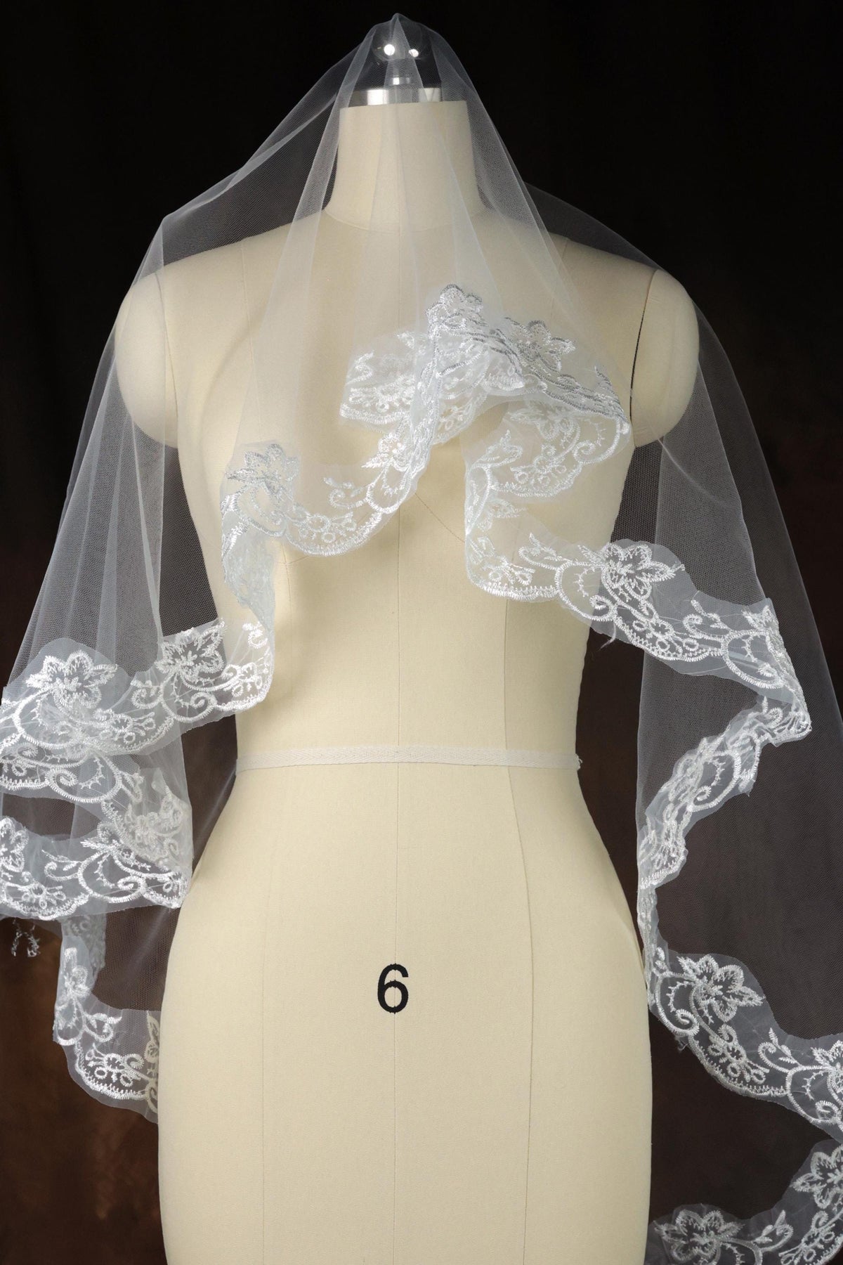 A mannequin wearing a white wedding veil with intricate lace detailing.