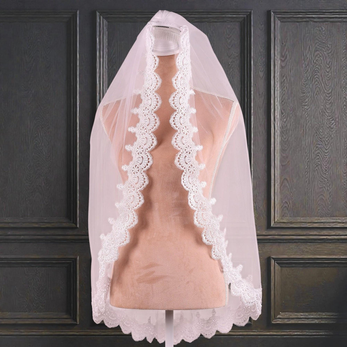 A white wedding veil with a delicate lace trim is displayed on a mannequin head against a dark background.